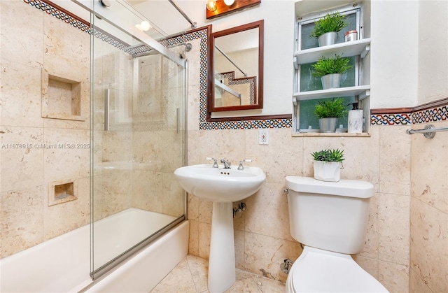 full bathroom with sink, toilet, shower / bath combination with glass door, and tile walls