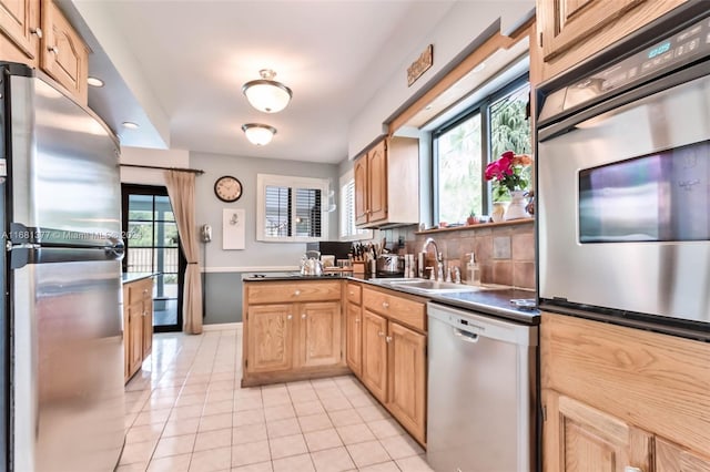 kitchen featuring light tile patterned floors, a sink, stainless steel appliances, baseboards, and backsplash
