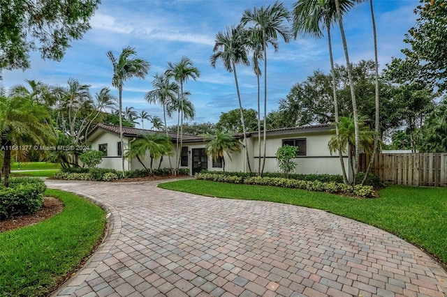 ranch-style home with stucco siding, fence, a front lawn, and curved driveway