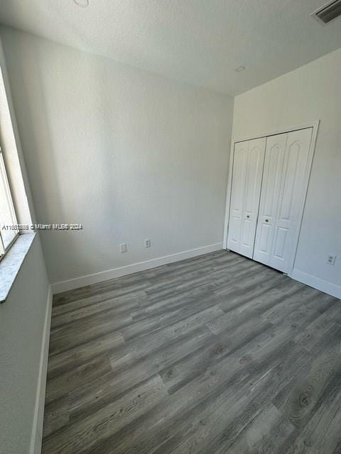 unfurnished bedroom featuring a closet, a textured ceiling, and dark hardwood / wood-style flooring