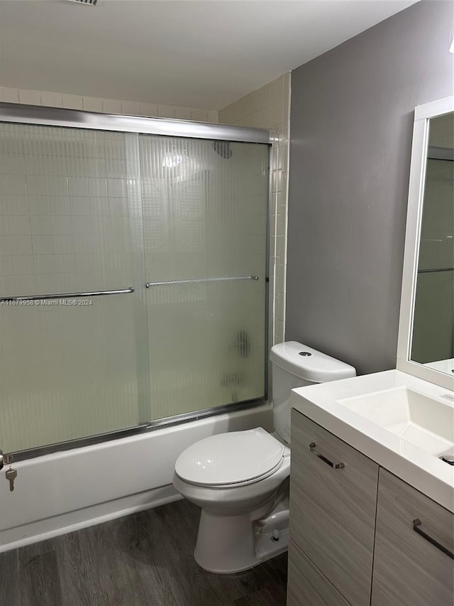 full bathroom featuring combined bath / shower with glass door, hardwood / wood-style floors, vanity, and toilet