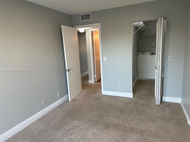 unfurnished bedroom with a walk in closet, light carpet, and a closet