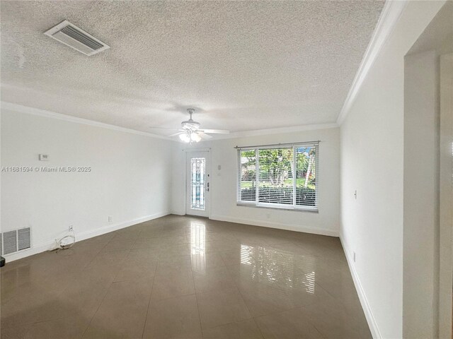 empty room featuring dark tile patterned floors, ornamental molding, a textured ceiling, and ceiling fan