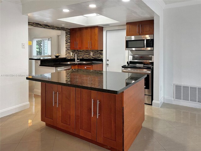 kitchen with appliances with stainless steel finishes, a kitchen island with sink, dark stone counters, light tile patterned flooring, and sink