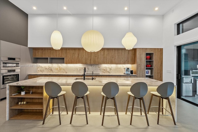 kitchen featuring an island with sink, sink, hanging light fixtures, and backsplash