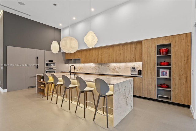 kitchen featuring a kitchen breakfast bar, an island with sink, backsplash, sink, and pendant lighting