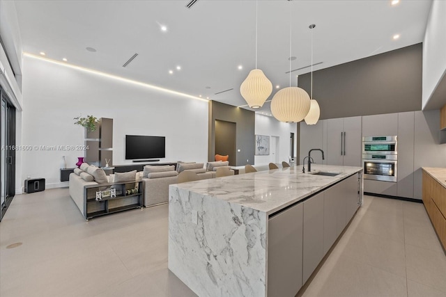 kitchen with a spacious island, double oven, sink, pendant lighting, and light stone counters