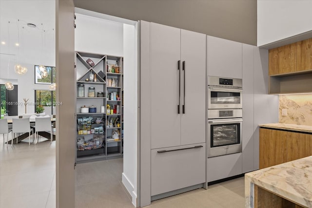 kitchen with white cabinets, light tile patterned flooring, a high ceiling, decorative light fixtures, and stainless steel double oven