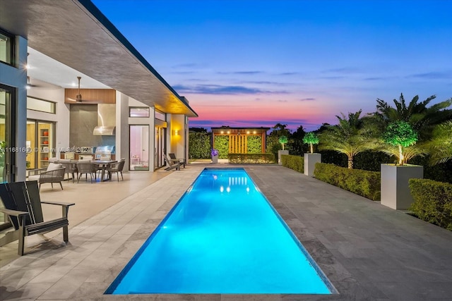 pool at dusk with a patio area and a grill