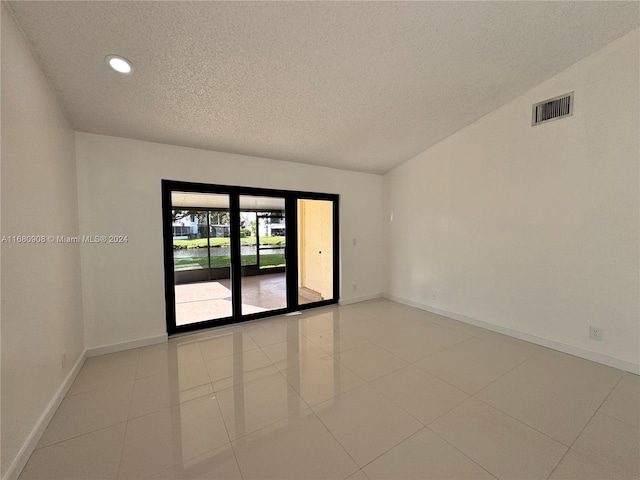 tiled empty room with a textured ceiling and vaulted ceiling