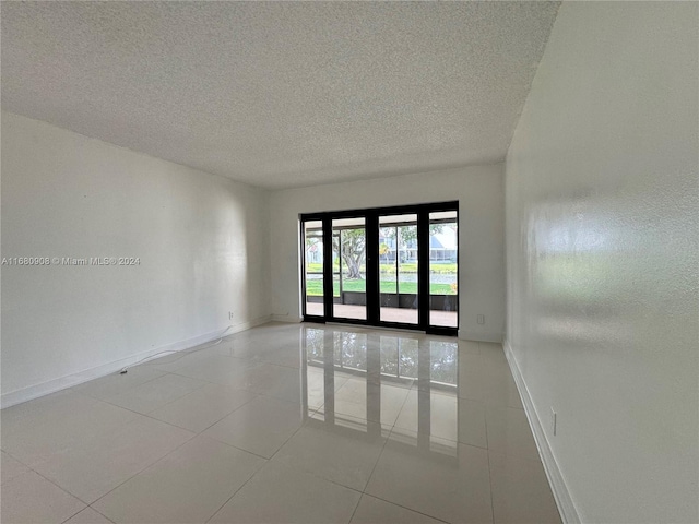 empty room featuring french doors, a textured ceiling, and light tile patterned floors