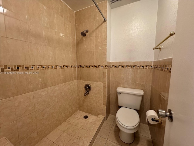 bathroom with a tile shower, toilet, tile patterned floors, and tile walls