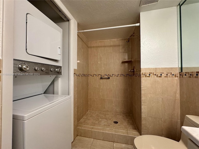 bathroom featuring tile walls, tiled shower, toilet, and stacked washing maching and dryer