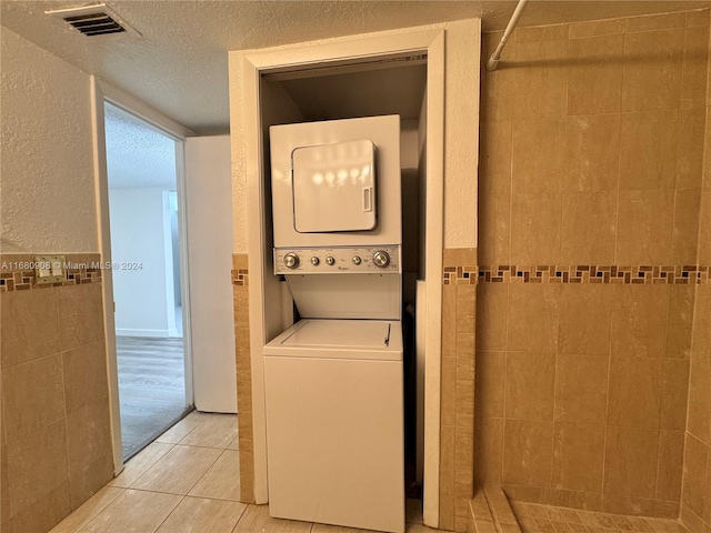 clothes washing area with stacked washer / dryer, tile walls, a textured ceiling, and light hardwood / wood-style floors