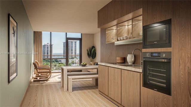 kitchen featuring oven, light brown cabinets, black microwave, floor to ceiling windows, and light hardwood / wood-style floors