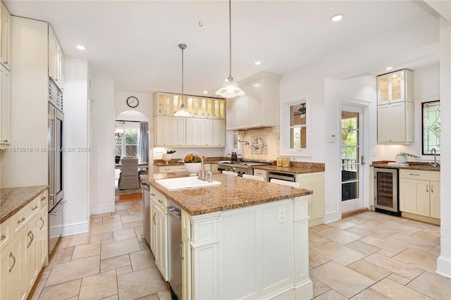 kitchen featuring beverage cooler, light stone counters, an island with sink, pendant lighting, and sink