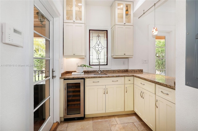 kitchen with kitchen peninsula, hanging light fixtures, dark stone counters, wine cooler, and sink