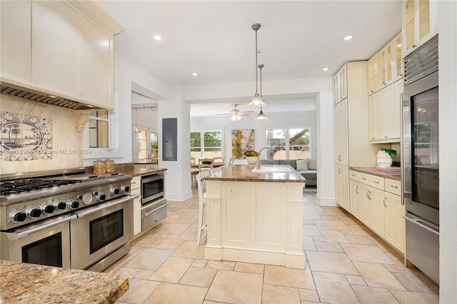 kitchen with an island with sink, stainless steel appliances, light stone countertops, pendant lighting, and ceiling fan