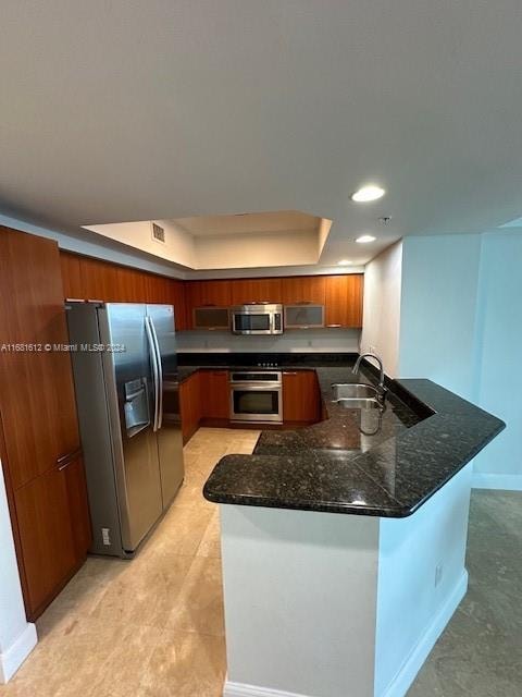 kitchen with sink, dark stone counters, stainless steel appliances, and a raised ceiling