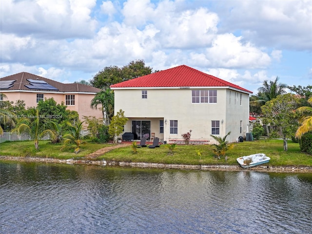 back of house with a water view and a lawn