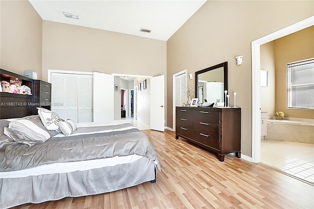 bedroom featuring ensuite bathroom, light wood-type flooring, high vaulted ceiling, and multiple closets