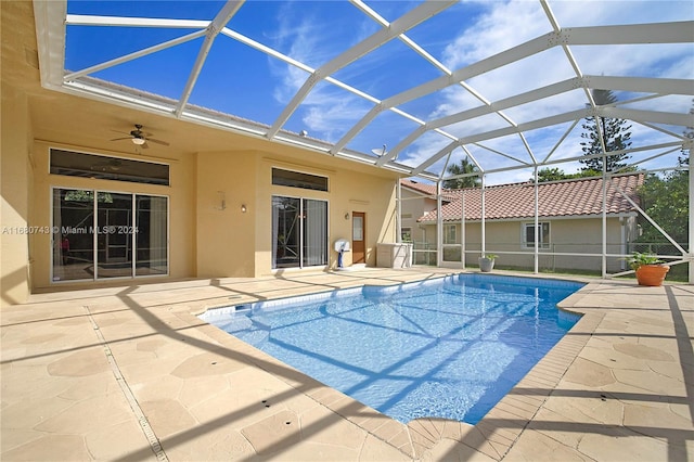 view of swimming pool with glass enclosure, ceiling fan, and a patio