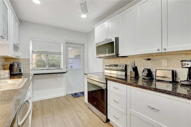 kitchen with white cabinetry, light wood-type flooring, dark stone counters, and appliances with stainless steel finishes