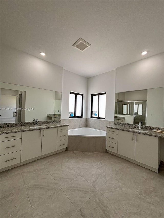 bathroom featuring a sink, visible vents, two vanities, and a garden tub