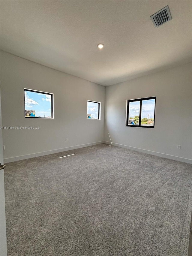 empty room with carpet flooring, baseboards, visible vents, and a wealth of natural light