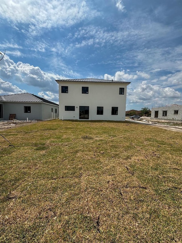 back of house with a yard, metal roof, and stucco siding