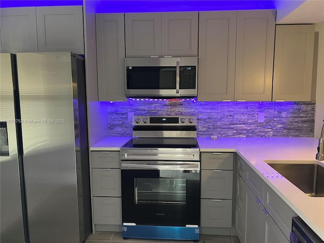 kitchen with appliances with stainless steel finishes, gray cabinetry, tasteful backsplash, and sink