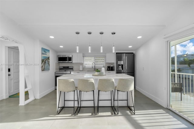 kitchen featuring appliances with stainless steel finishes, a center island, white cabinetry, decorative light fixtures, and a breakfast bar area