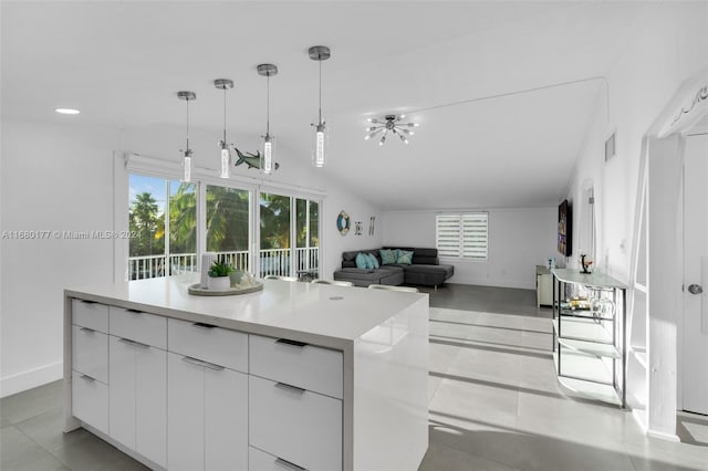 kitchen featuring white cabinets, hanging light fixtures, light tile patterned floors, vaulted ceiling, and a center island