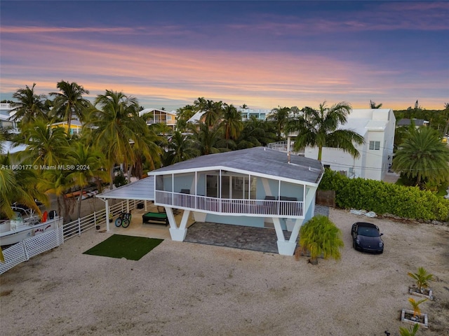 back house at dusk with a sunroom and a carport