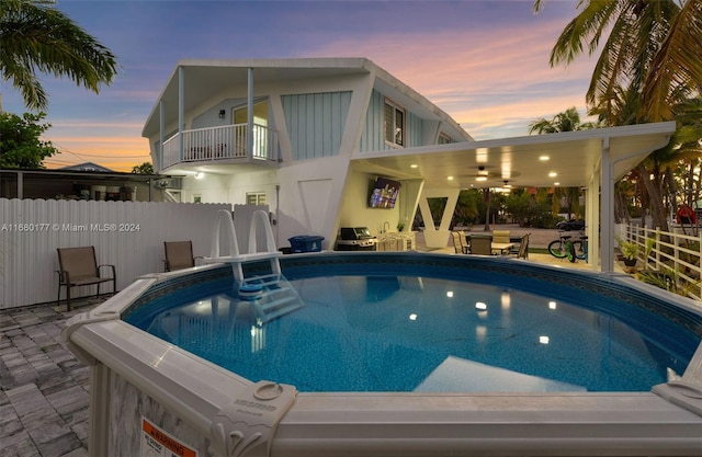 pool at dusk with a patio area and ceiling fan