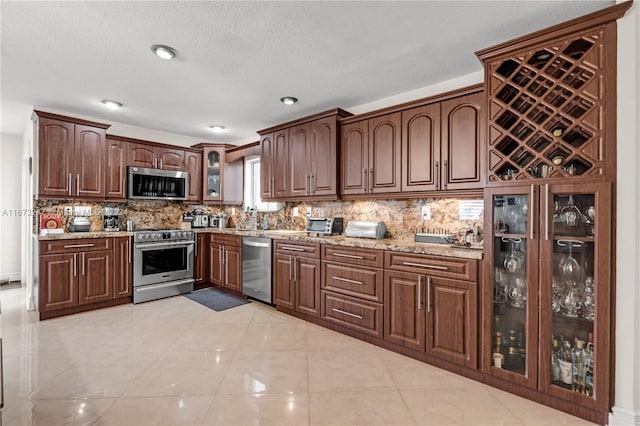 kitchen with tasteful backsplash, appliances with stainless steel finishes, a textured ceiling, light stone countertops, and light tile patterned flooring