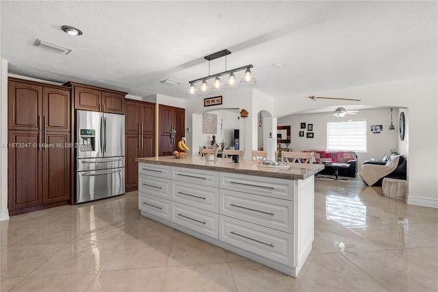 kitchen featuring an island with sink, hanging light fixtures, stainless steel fridge with ice dispenser, a textured ceiling, and ceiling fan