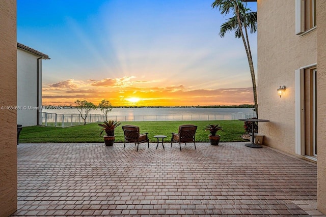 patio terrace at dusk featuring a water view and a lawn