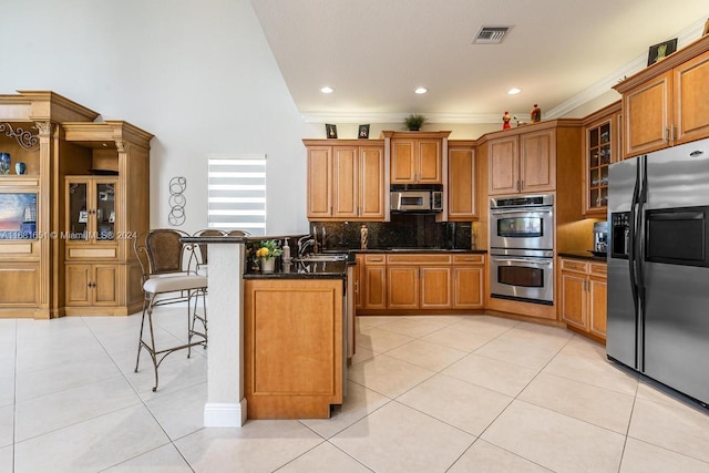 kitchen with appliances with stainless steel finishes, backsplash, a breakfast bar area, ornamental molding, and light tile patterned floors