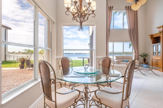 dining area featuring light tile patterned flooring, a water view, and ceiling fan with notable chandelier