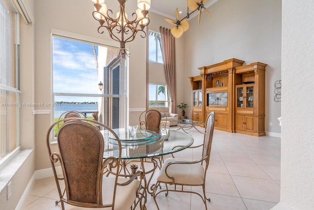 dining space with a chandelier, light tile patterned flooring, a towering ceiling, crown molding, and a water view