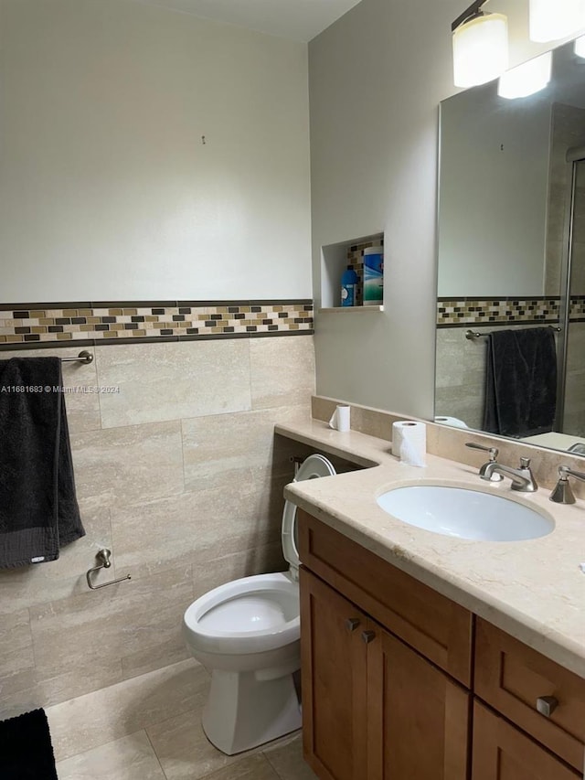 bathroom featuring vanity, toilet, a shower, and tile walls