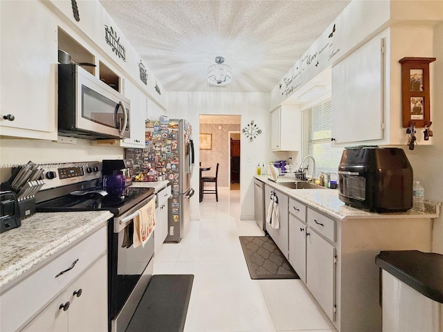 kitchen with appliances with stainless steel finishes, sink, a textured ceiling, white cabinetry, and light tile patterned floors