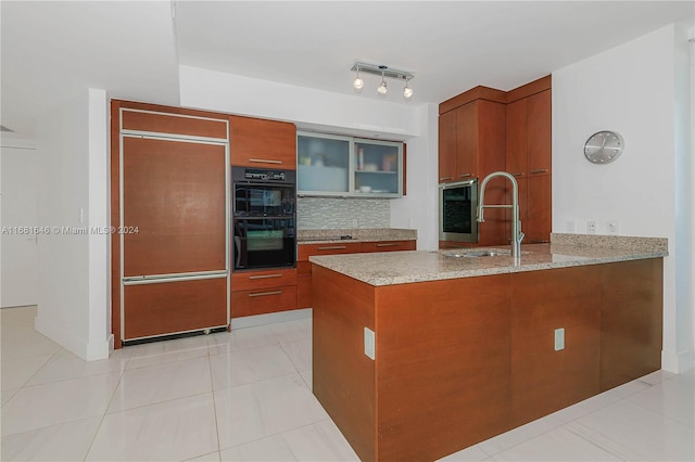 kitchen with sink, light stone counters, backsplash, paneled built in fridge, and double oven