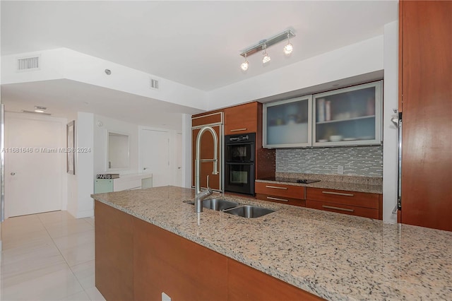 kitchen with track lighting, light stone countertops, light tile patterned floors, black double oven, and decorative backsplash