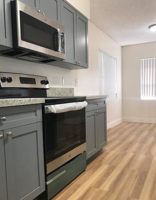 kitchen featuring stainless steel appliances, light hardwood / wood-style floors, and gray cabinetry