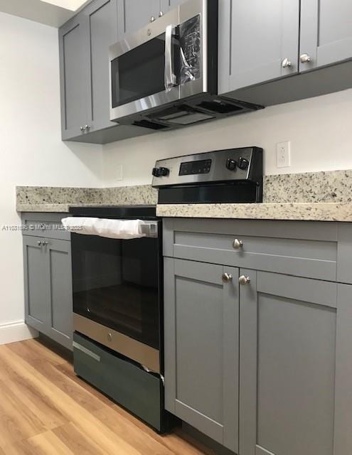 kitchen with light stone counters, appliances with stainless steel finishes, light hardwood / wood-style floors, and gray cabinetry