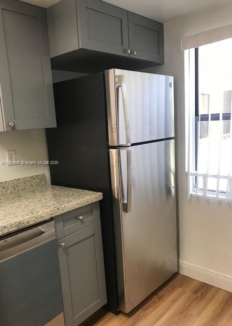 kitchen with stainless steel appliances, plenty of natural light, light stone counters, and light hardwood / wood-style flooring