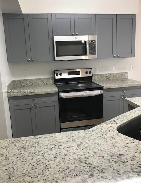 kitchen featuring light stone counters, gray cabinets, and stainless steel appliances