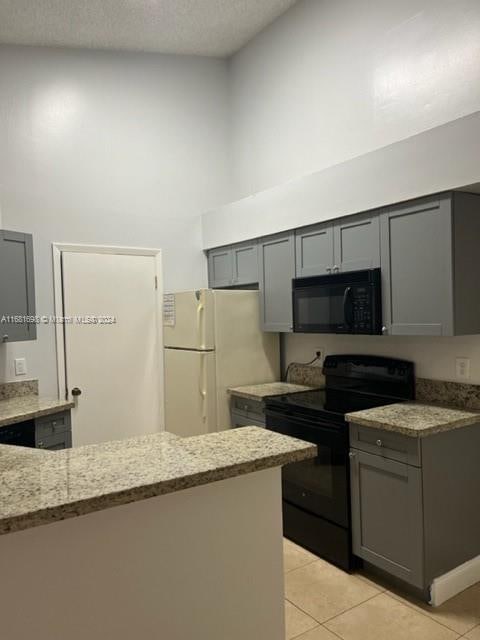 kitchen with black appliances, light stone countertops, light tile patterned floors, gray cabinets, and a textured ceiling